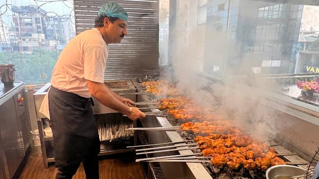 A Peshawari Kitchen chef grilling skewers over open flame